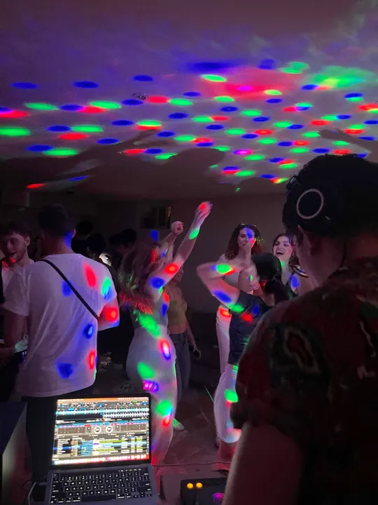 DJ DJ in headphones behind the laptop as a crowd dances under coloured disco lights