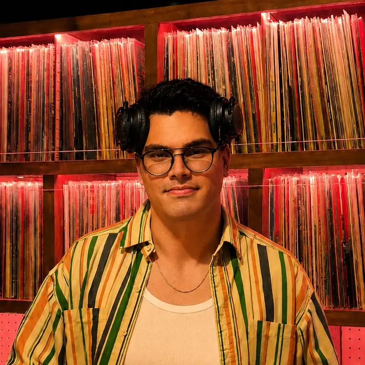 DJ DJ in a striped shirt in front of shelves of records
